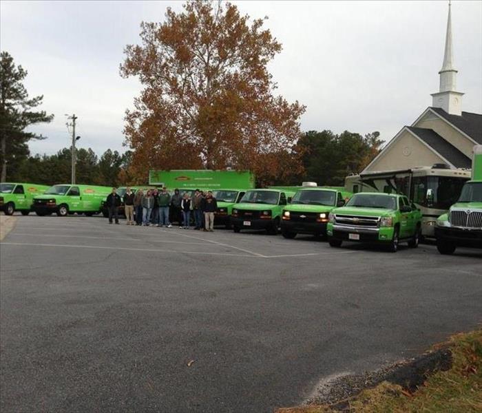 A lot of SERVPRO vehicles parked in front of church with employees standing in front of them 