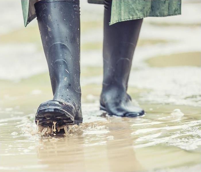 a person with black rain boots walking through flooded water 